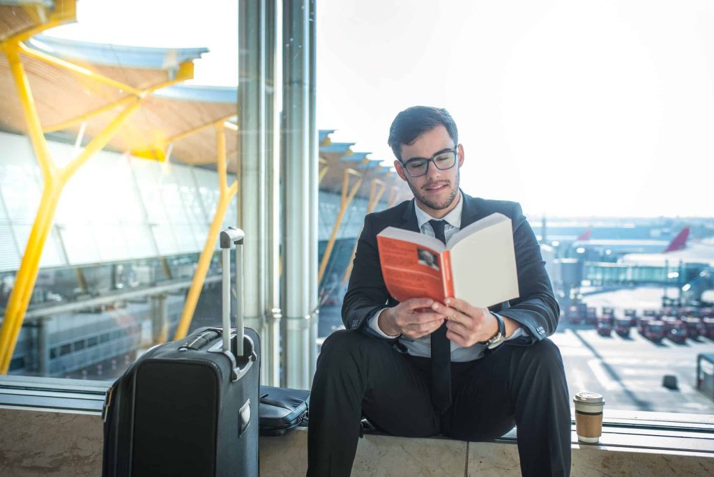 handsome businessman reading a book in the airport sitting close to the window
