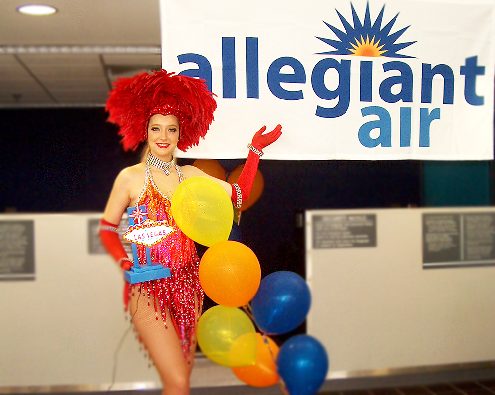 Vegas showgirl standing pointing to Allegiant Air banner