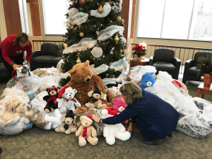 In the foreground of this photo, two hospital workers touch bags of bears that are all bundled sitting on the floor. 