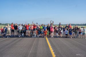 Front shot of a runway at South Bend International Airport. There is a group of people standing on the runway, jumping into the air with their hands and arms raised overhead.